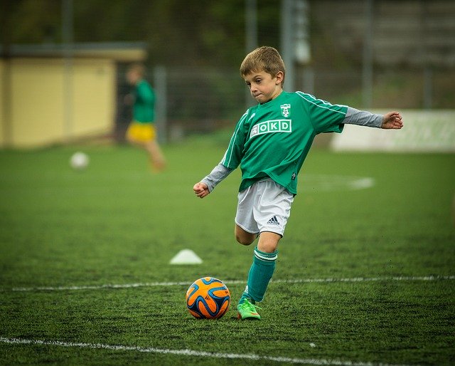 Chlapec v zelenom drese kope do futbalovej lopty.jpg